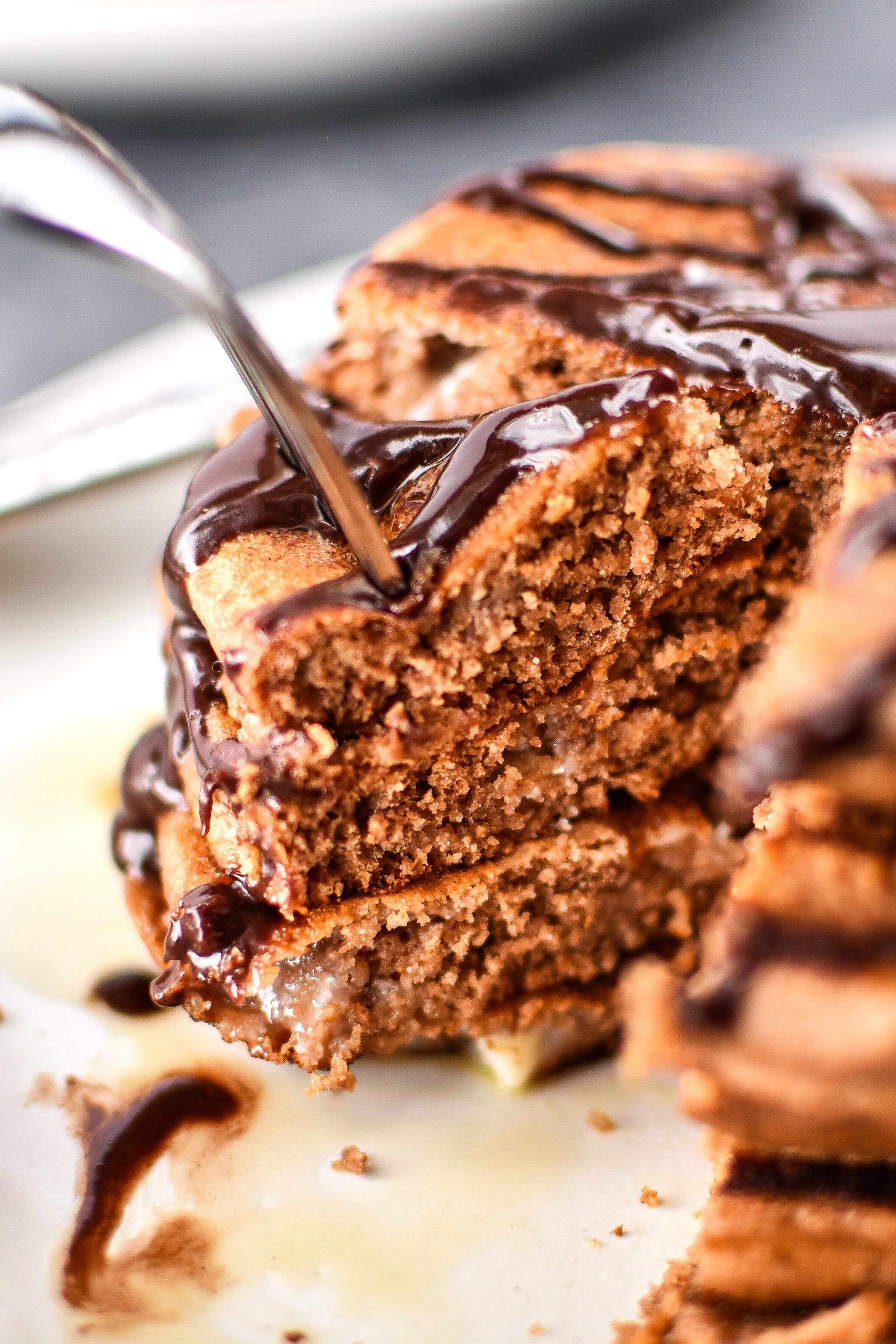 A fork piercing a big stack of Double Chocolate Peppermint Protein Pancakes drizzled with chocolate syrup.