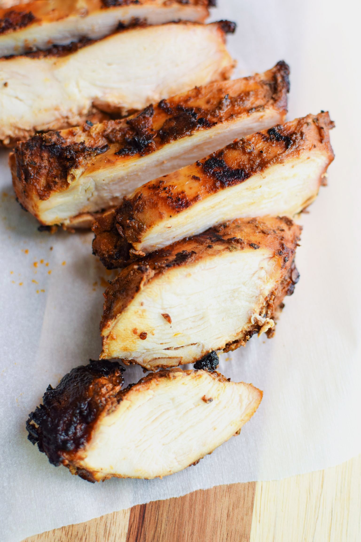 Grilled chicken breast cut into slices on a cutting board.