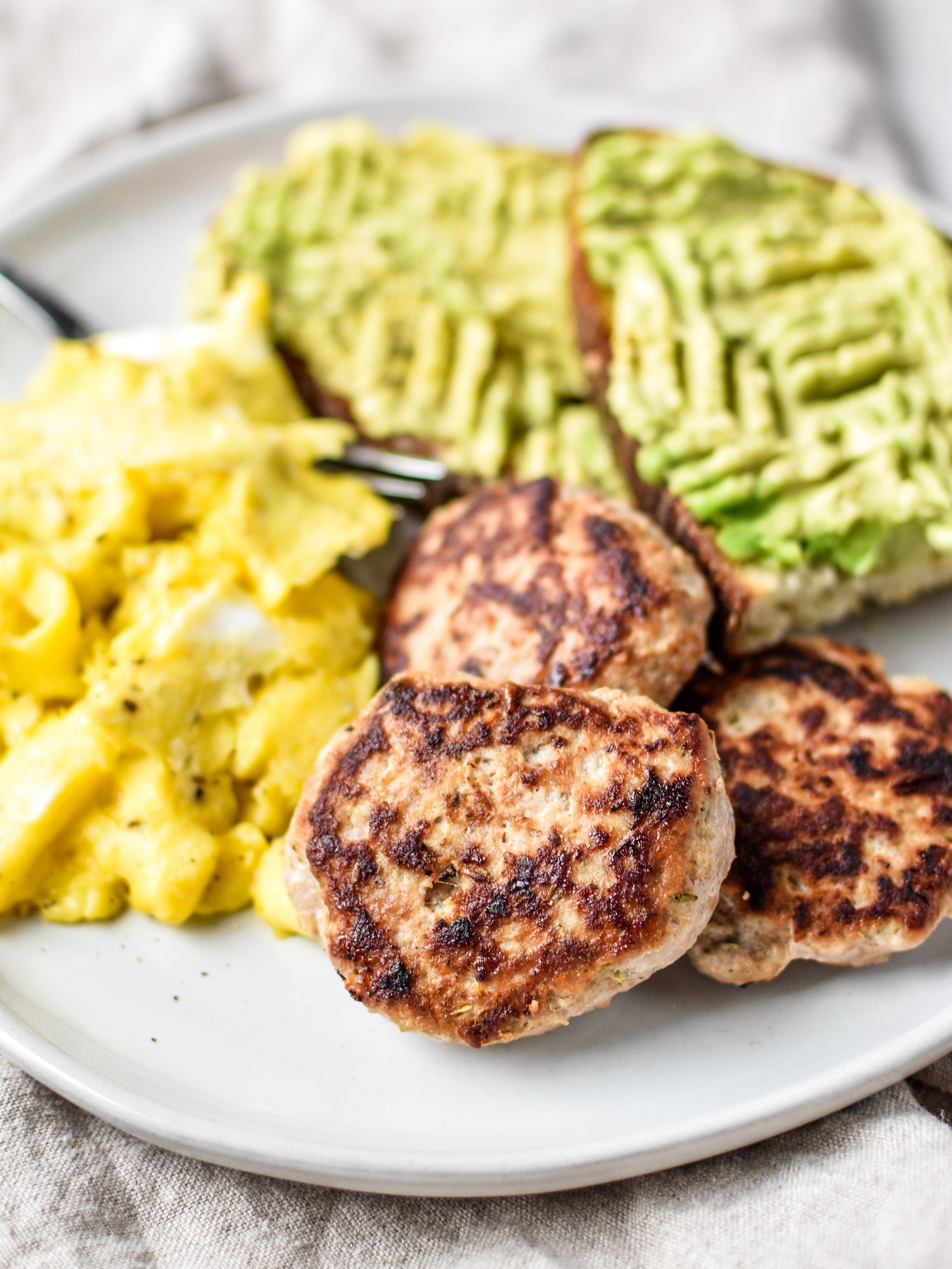 A plate of ground turkey breakfast sausage patties with eggs and avocado toast.