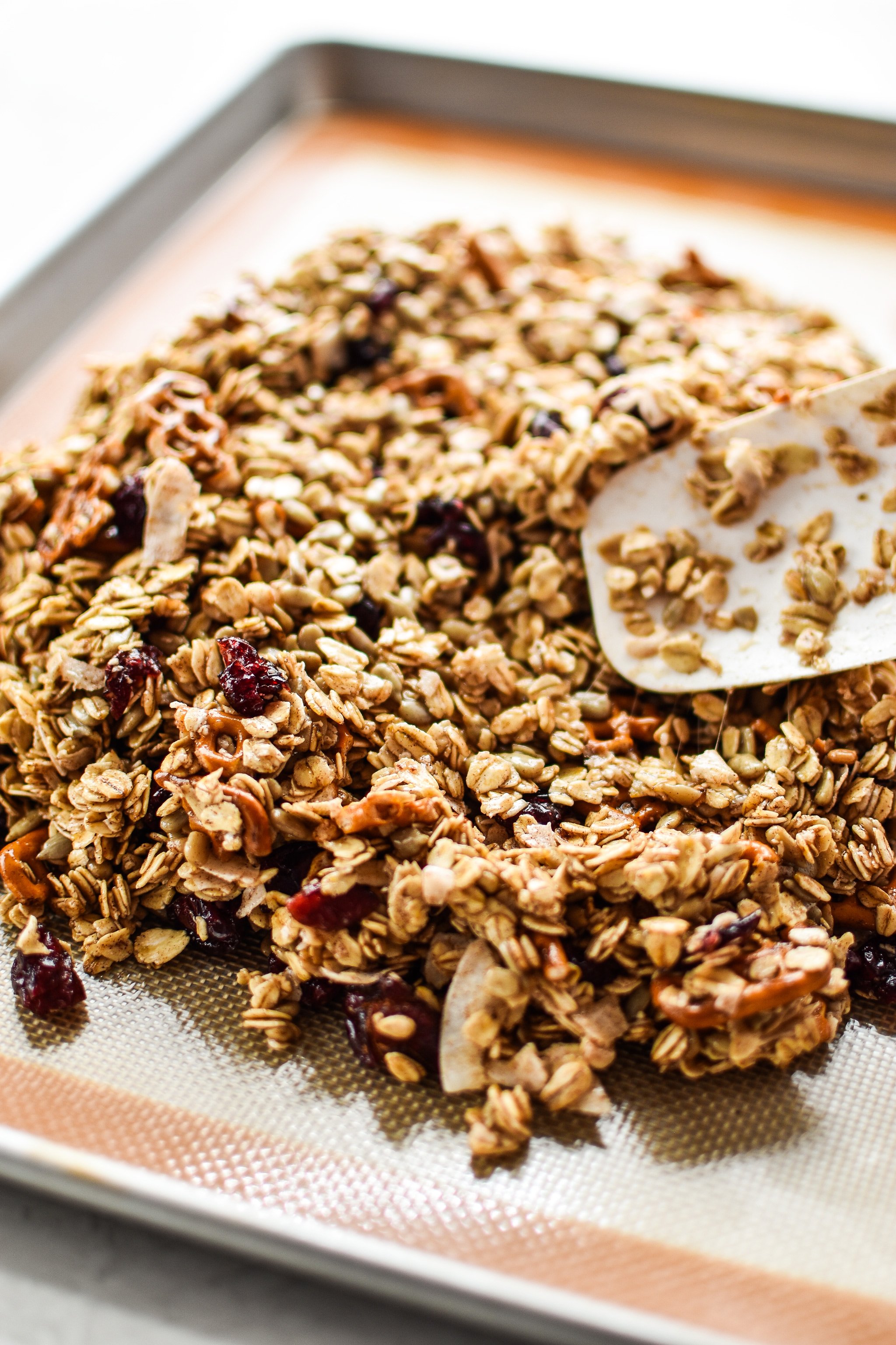 Using a spatula to spread the granola mixture on the sheet tray.