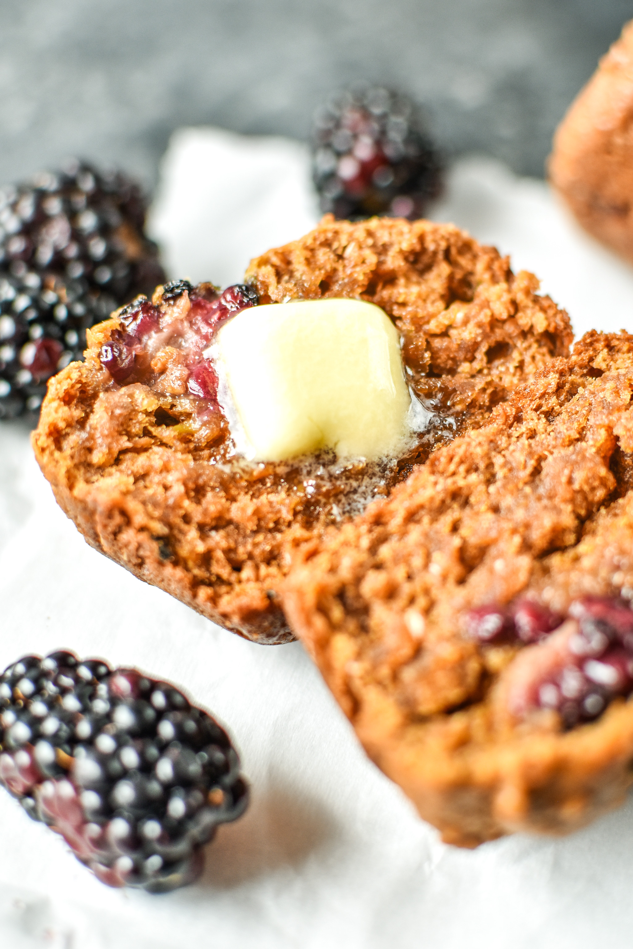 A slab of butter melting on a fresh baked blackberry bran muffin.