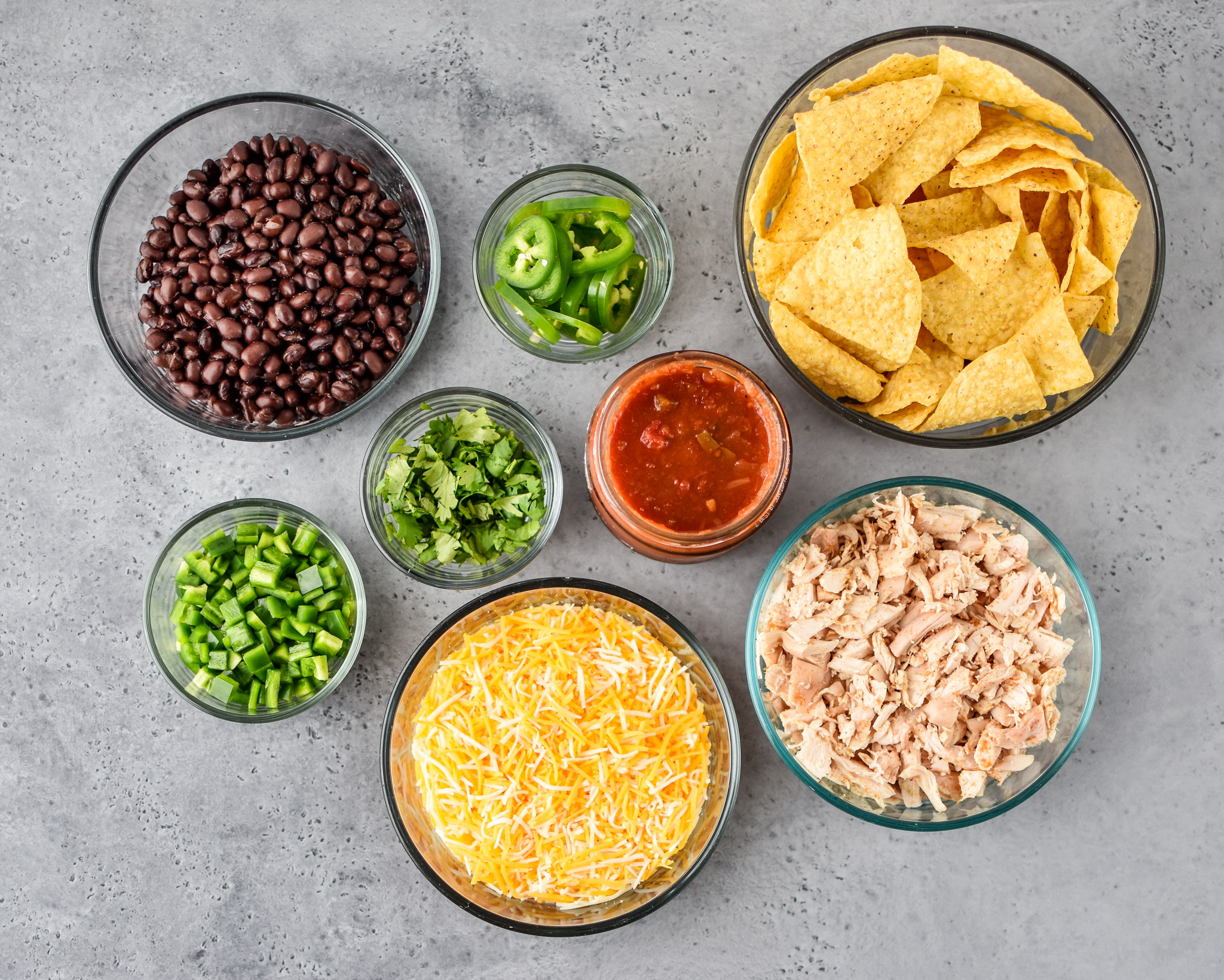 Components of the make ahead rotisserie chicken nachos stored in pyrex meal prep containers of various sizes.