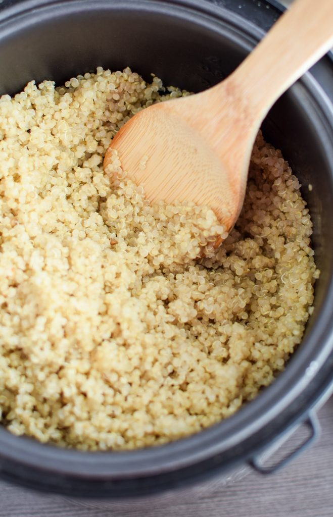 cooked quinoa in a rice cooker with a wooden spatula to scoop.