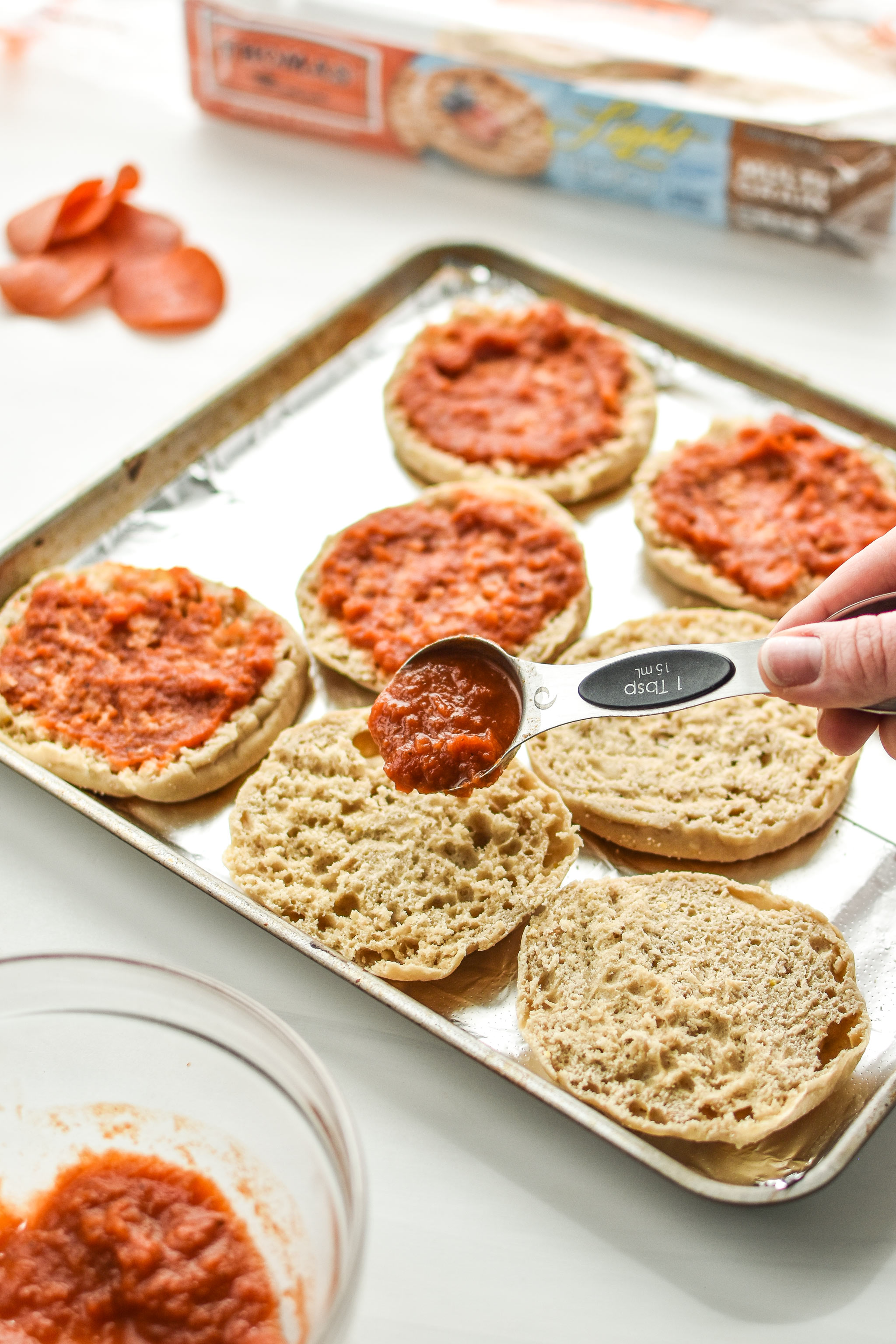 Adding sauce to the english muffins for the english muffin mini pizza meal prep