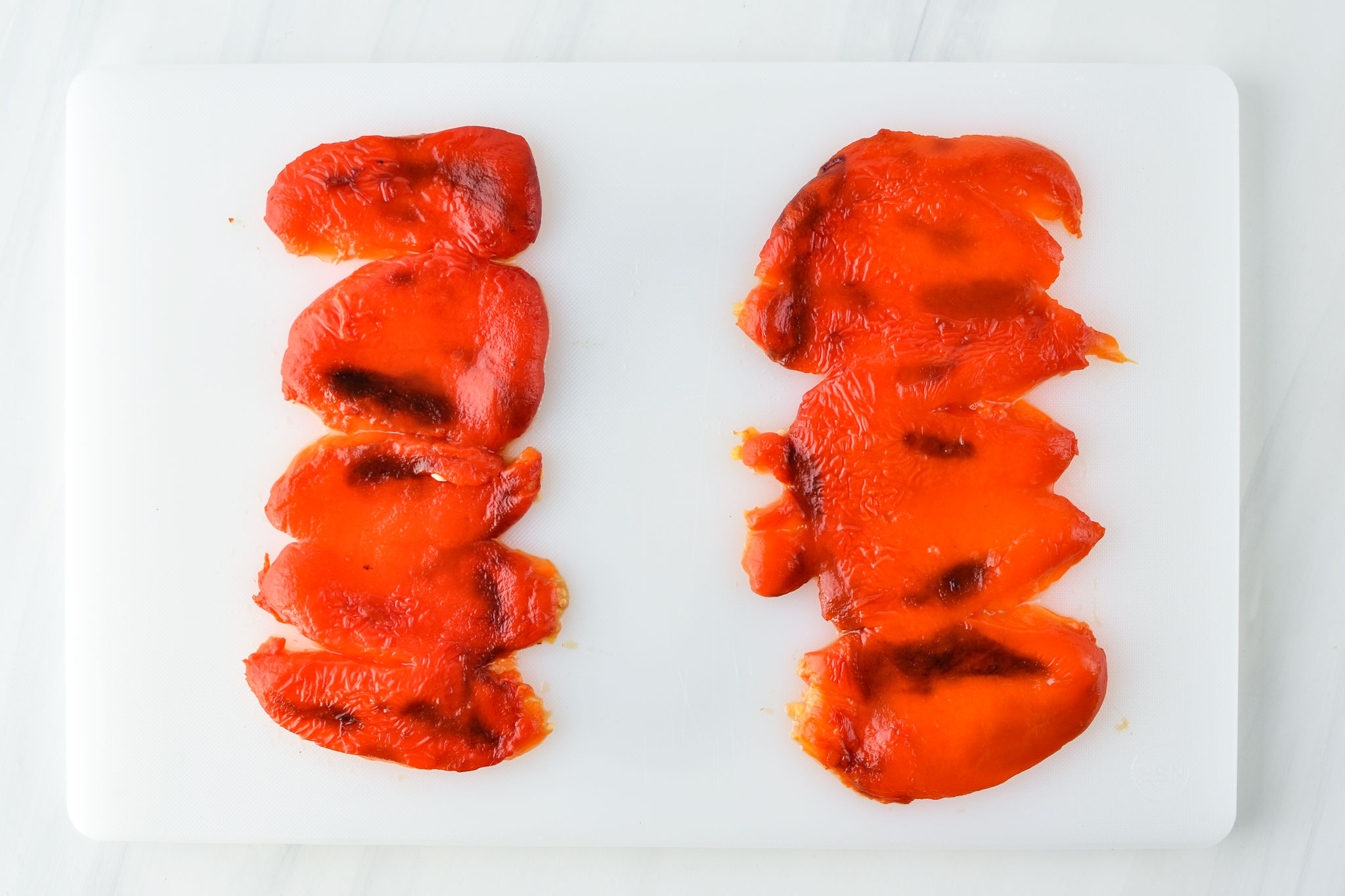 two red bell peppers roasted with stem, seeds and peel removed, laid out on a cutting board