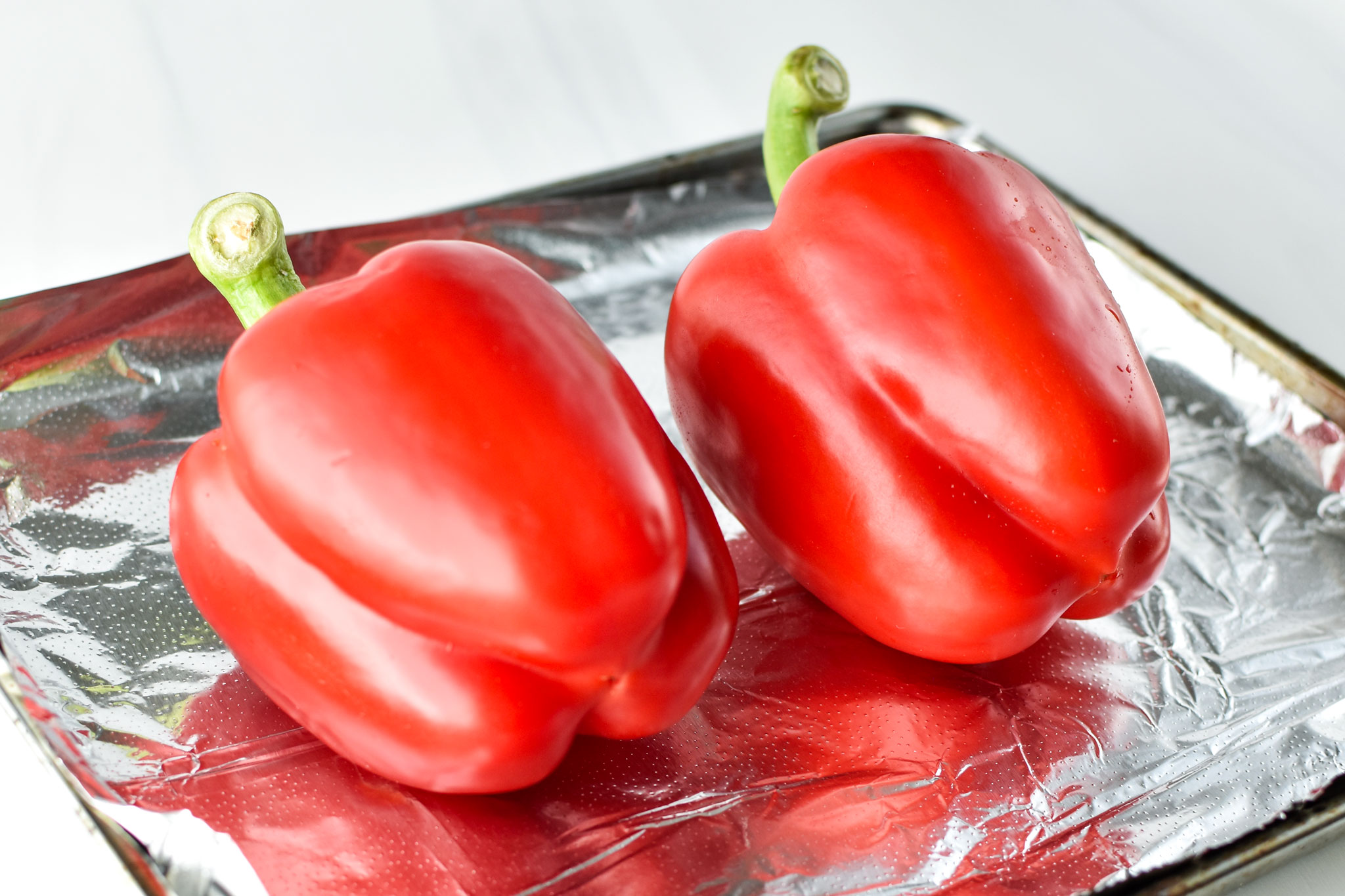 two raw red bell peppers on a sheet pan