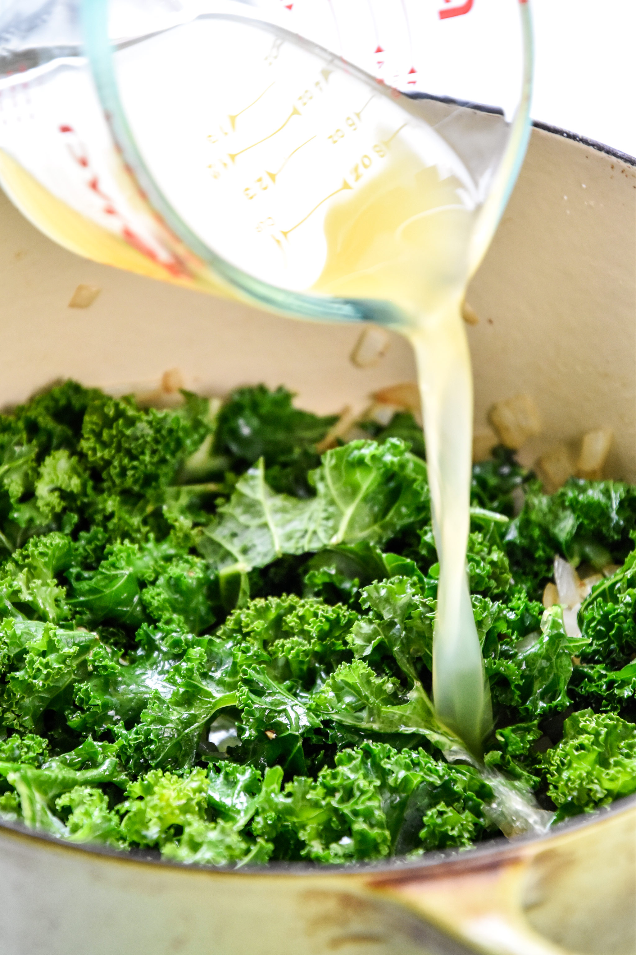 pouring broth into the pan with cooking kale