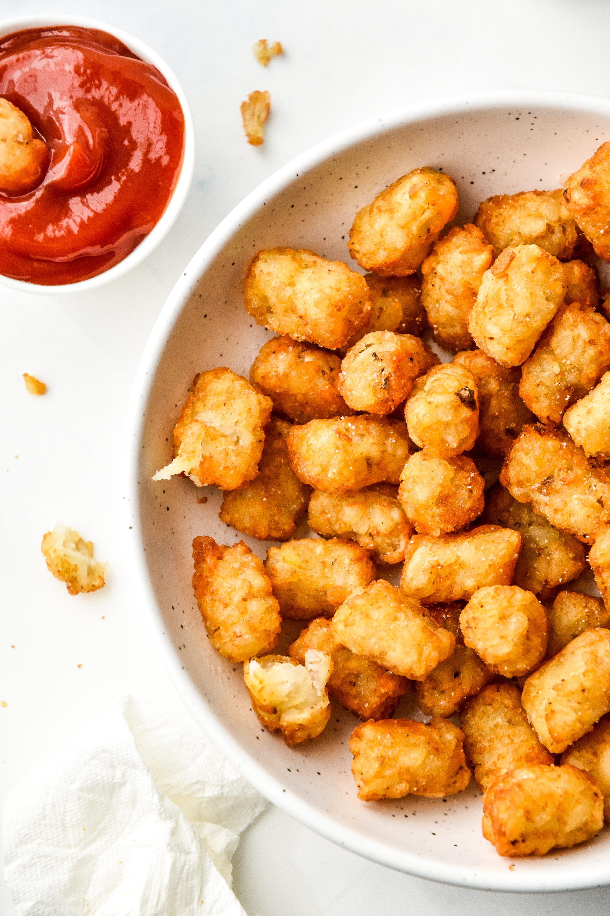 tater tots cooked in an air fryer served with ketchup in a bowl