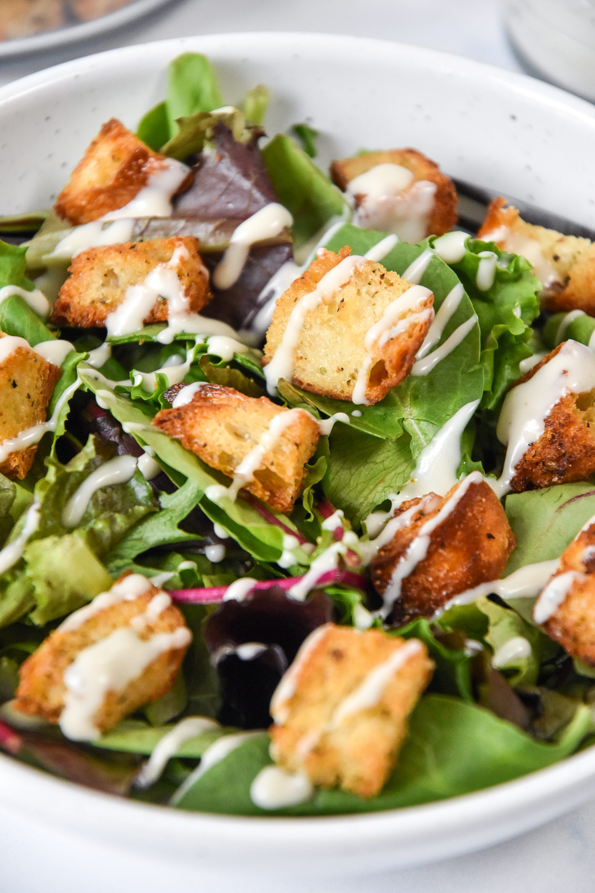 homemade croutons on top of a green salad with ranch drizzle.