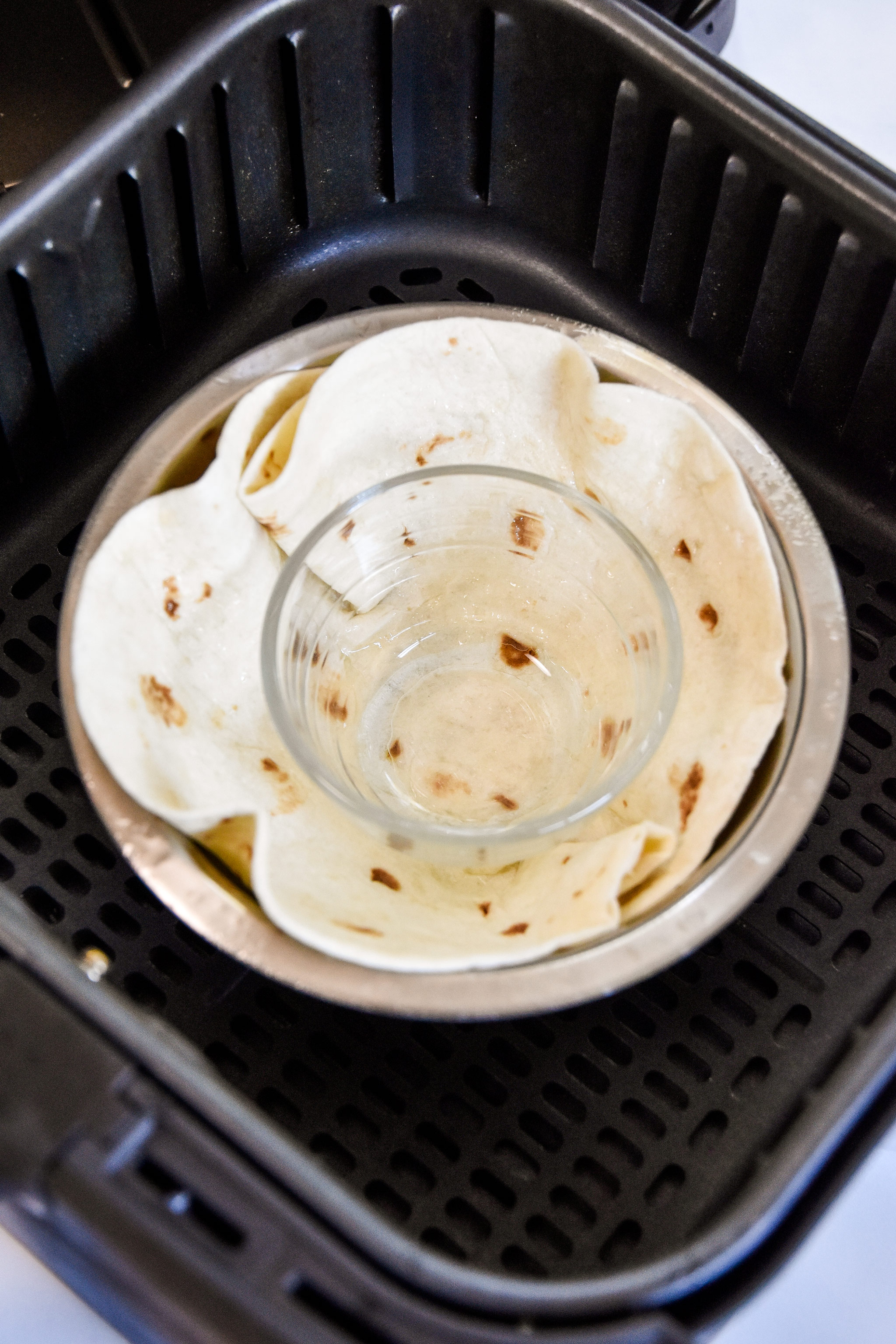 a flour tortilla between two bowls acting as a mold in an air fryer.