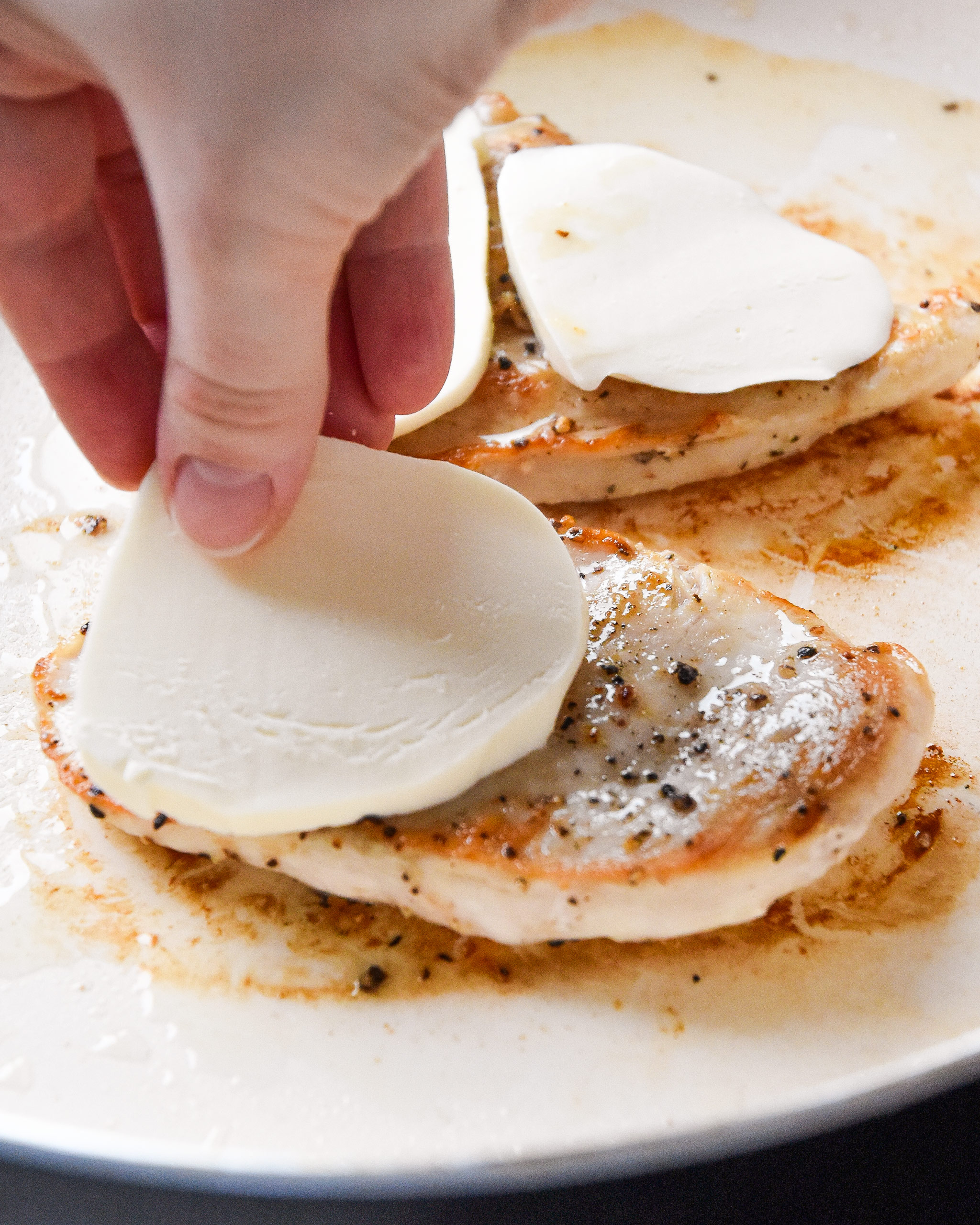 putting mozzarella cheese on the cooking chicken breast.