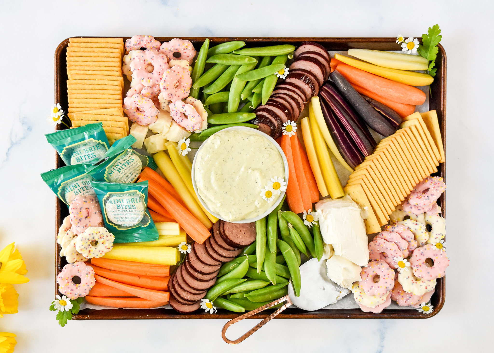 easy trader joes spring snack board finished with flowers and tons of veggies, crackers and cheese.