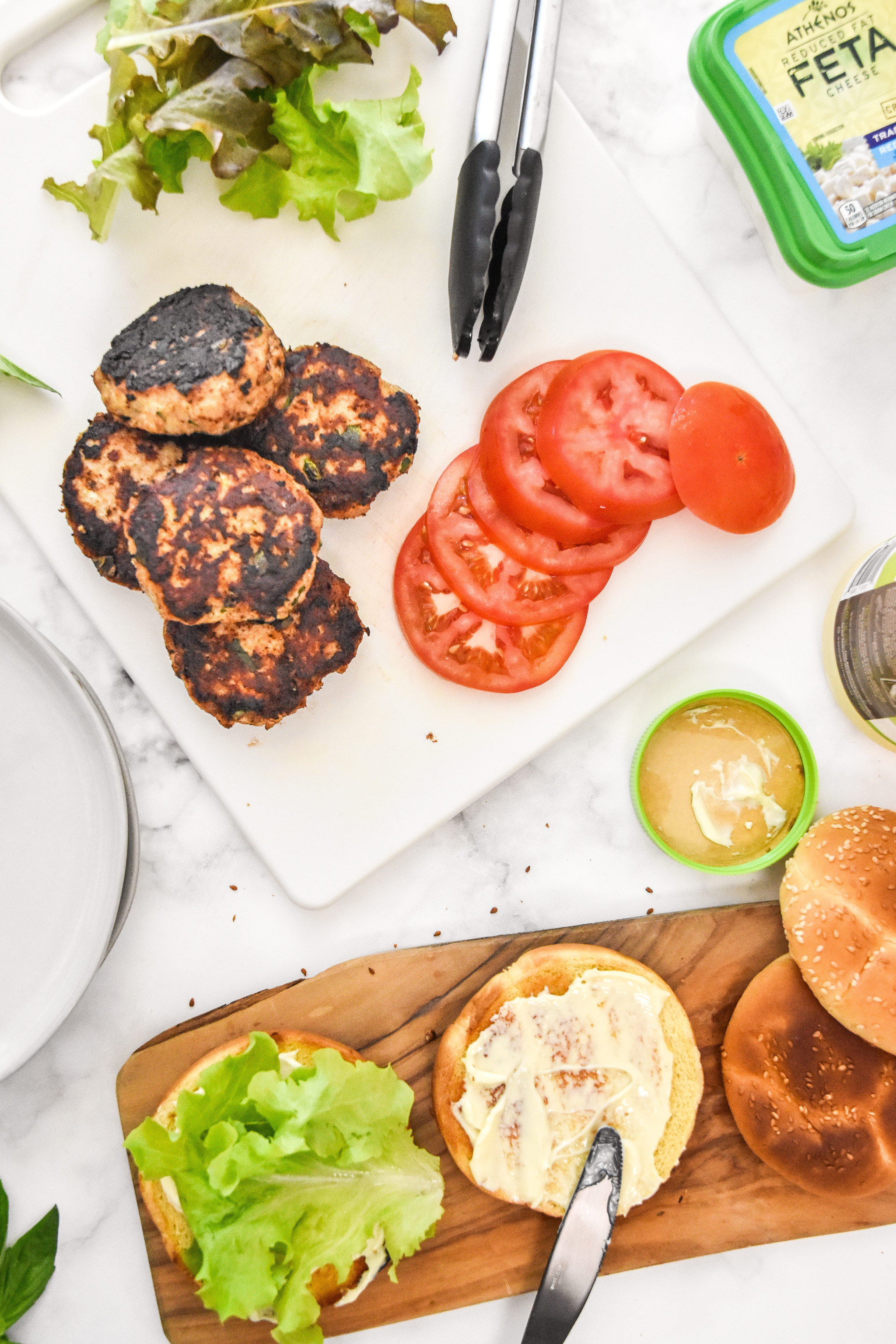 burger toppings, cooked burgers and buns on cutting boards.