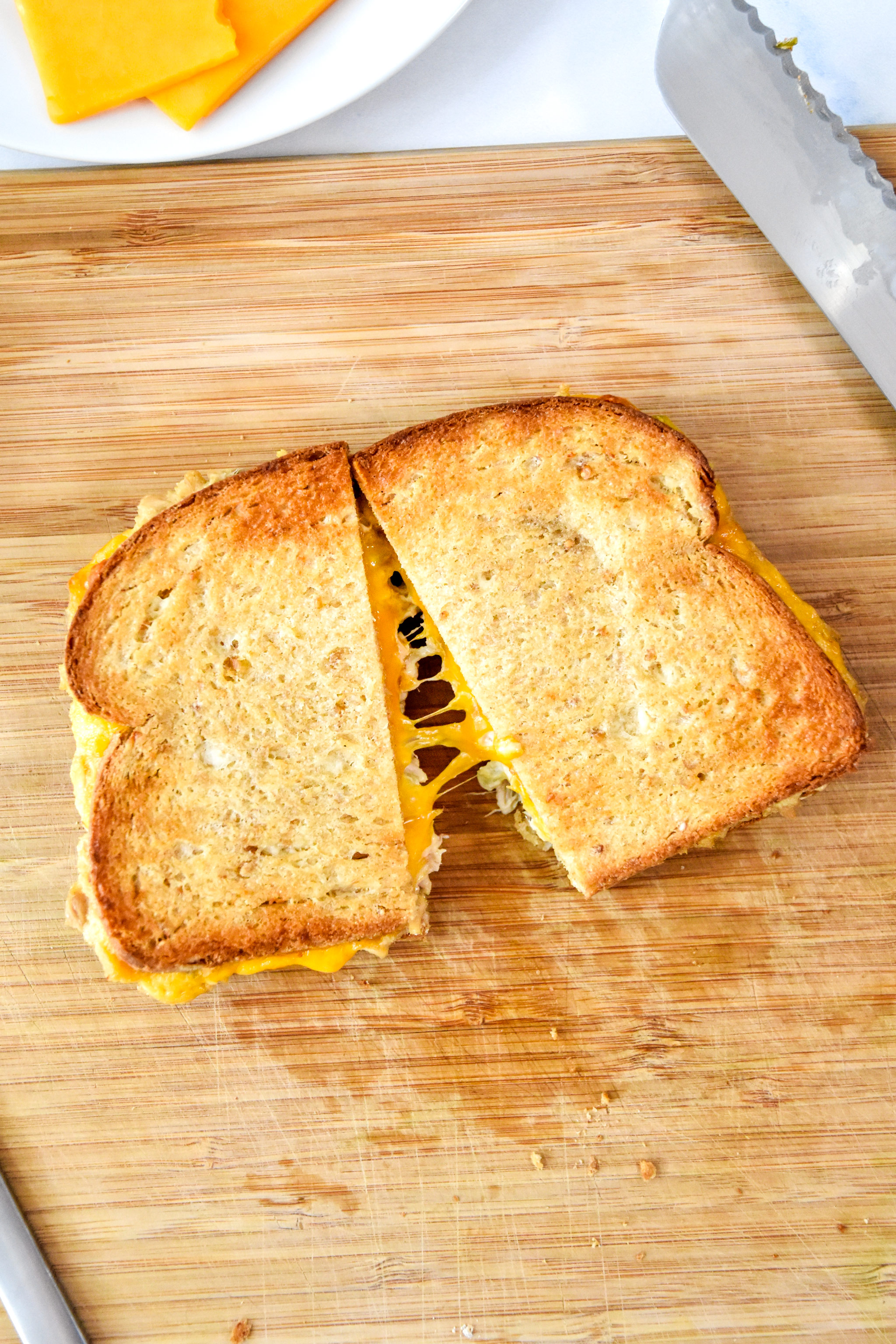 air fryer tuna melt cut in half on the cutting board, with a cheese pull.