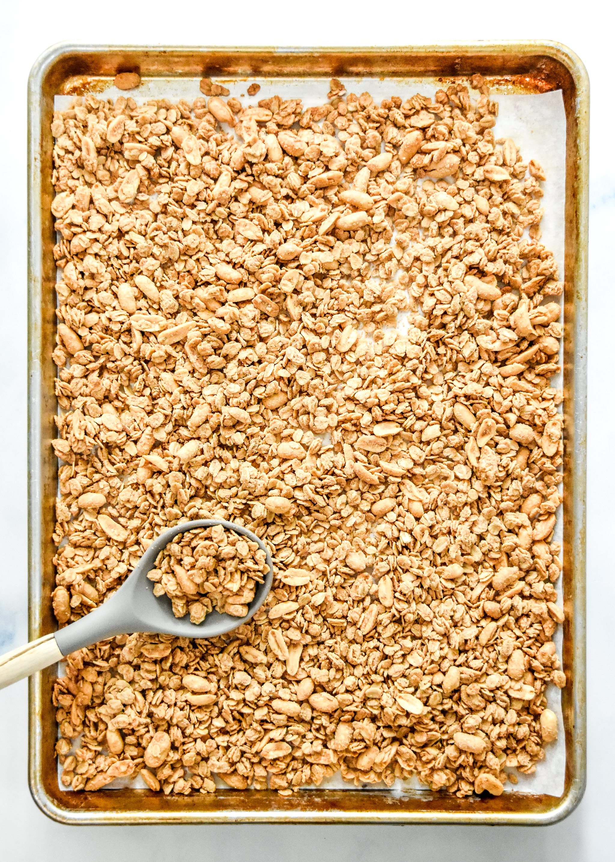 cooked peanut butter granola on a sheet pan with a spoon.