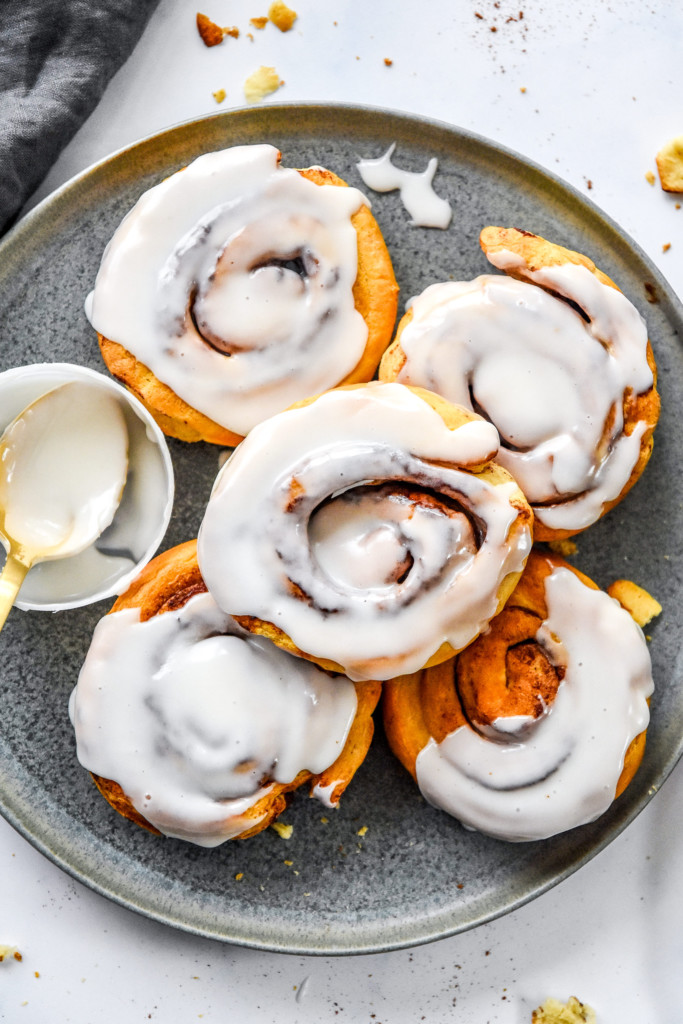 5 air fryer canned cinnamon rolls on a plate with frosting.