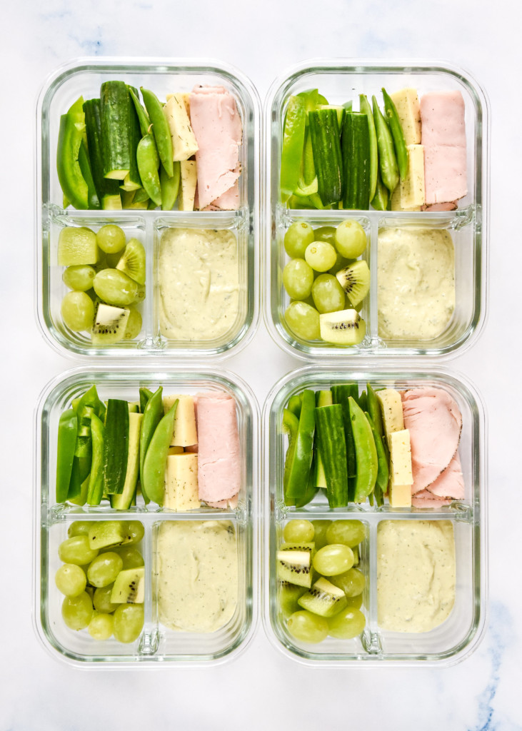 four glass containers of green food lunch box meal prep.