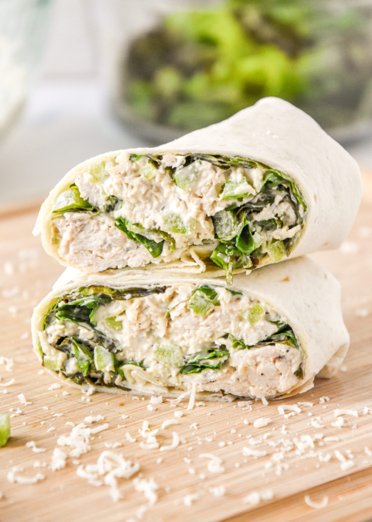 caesar chicken salad lunch wraps cut in half stacked on a cutting board.