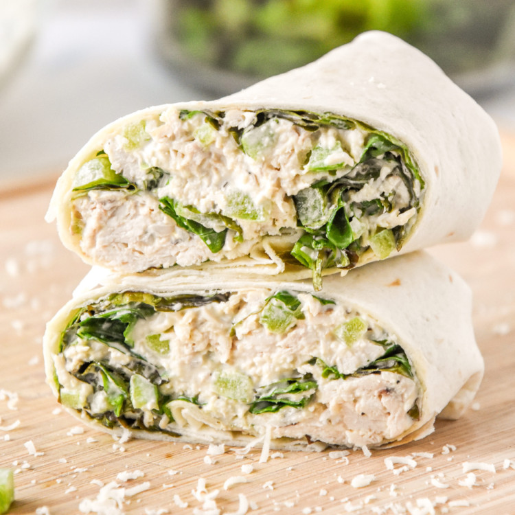caesar chicken salad lunch wraps cut in half stacked on a cutting board.