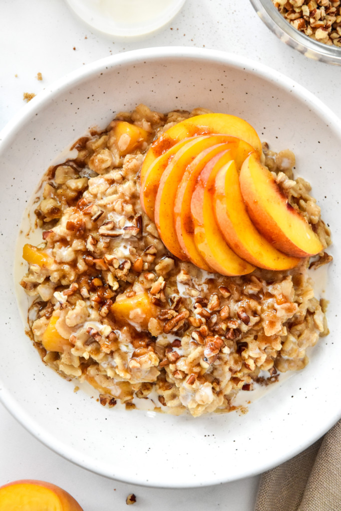peaches and cream oatmeal in a bowl with fresh peaches and pecans on top.