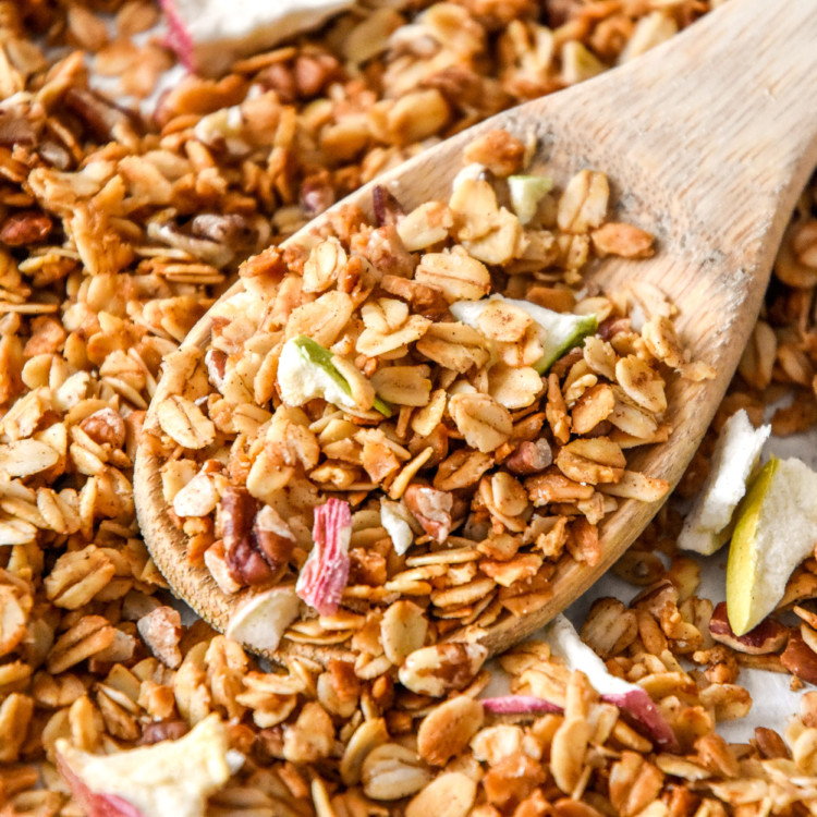 homemade apple pie spiced granola on a sheet pan with wooden spoon.
