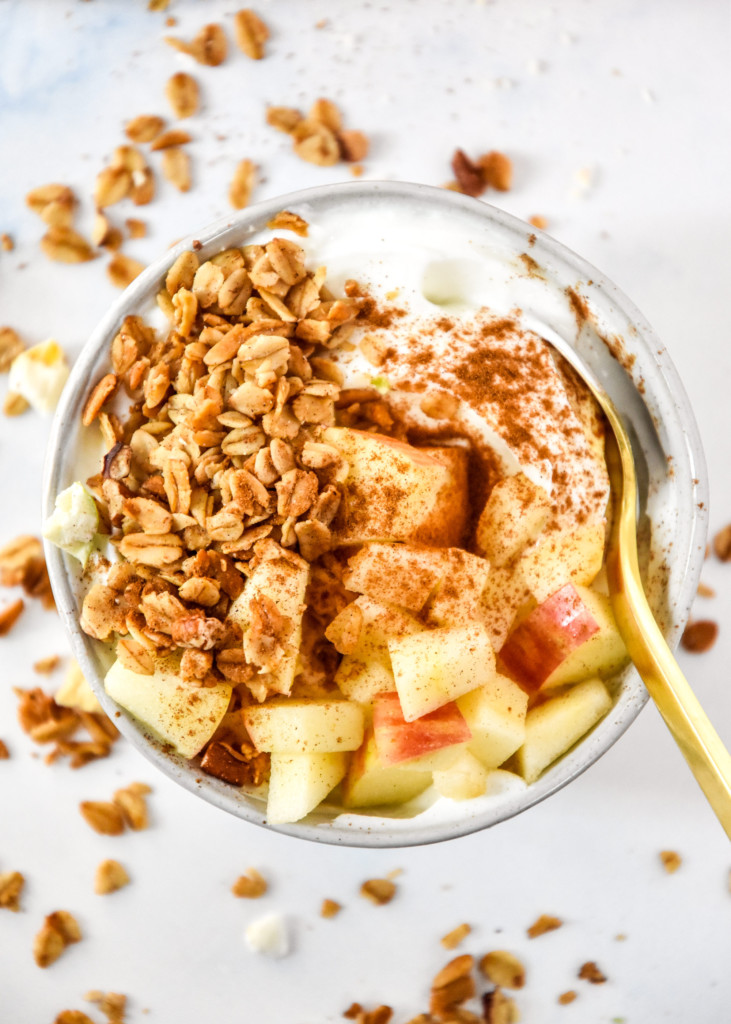 bowl of yogurt, diced apple and homemade apple pie spiced granola with a spoon.