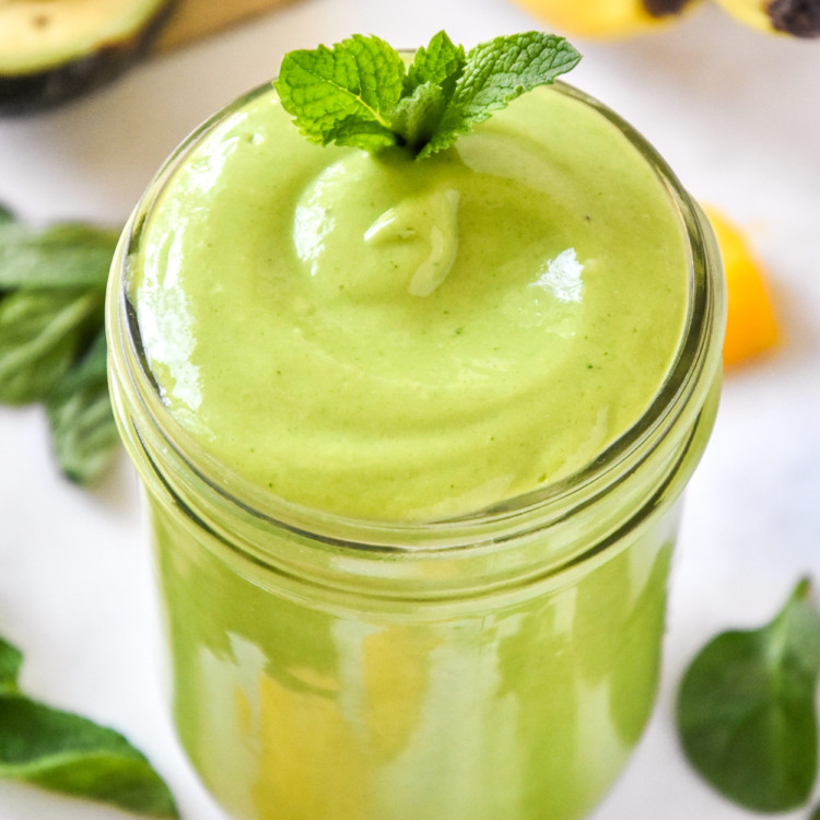 creamy avocado mint green smoothie in a mason jar with a mint leaf on top.