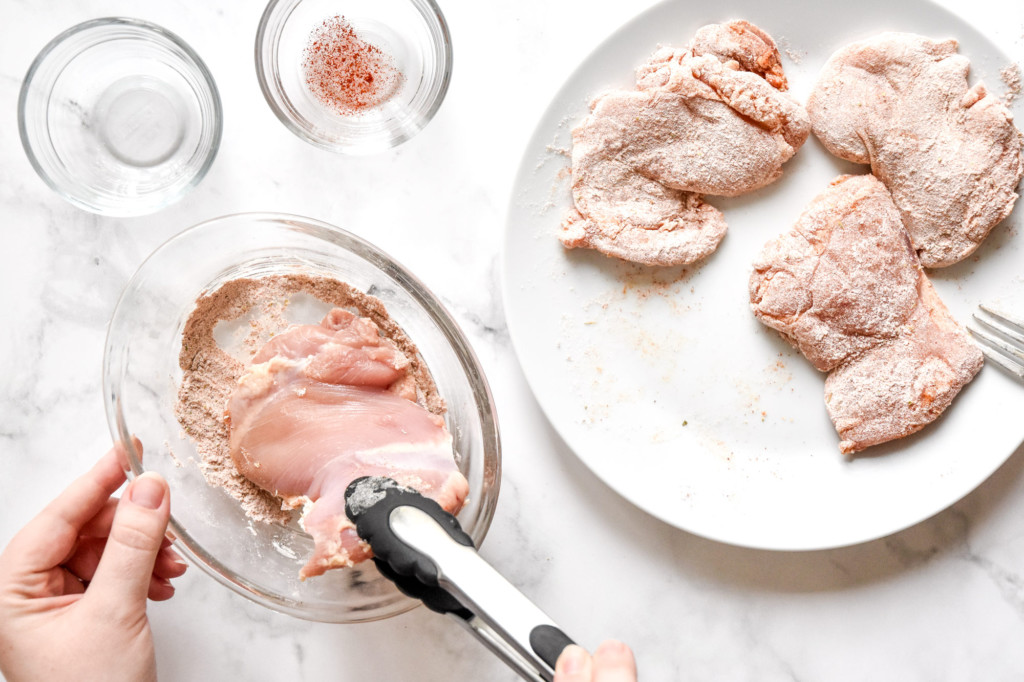 coating chicken thighs in flour seasoning mixture and staging on a white plate.