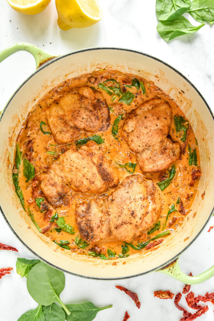creamy tuscan chicken meal prep with chicken thighs in a creamy sauce in a dutch oven.