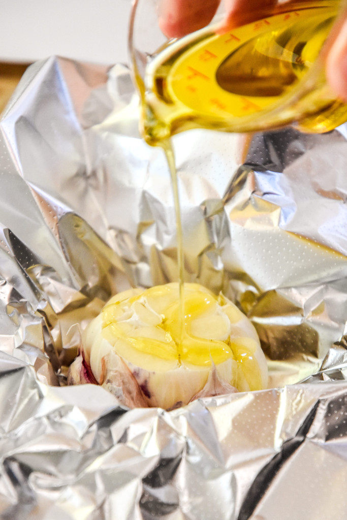 pouring oil on a head of garlic in foil in preparation to roast in an air fryer.