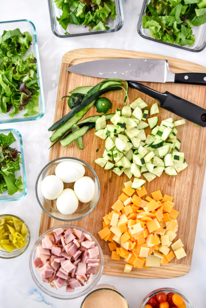 prepping and cutting all the ingredients for the chef salad on a cutting board.