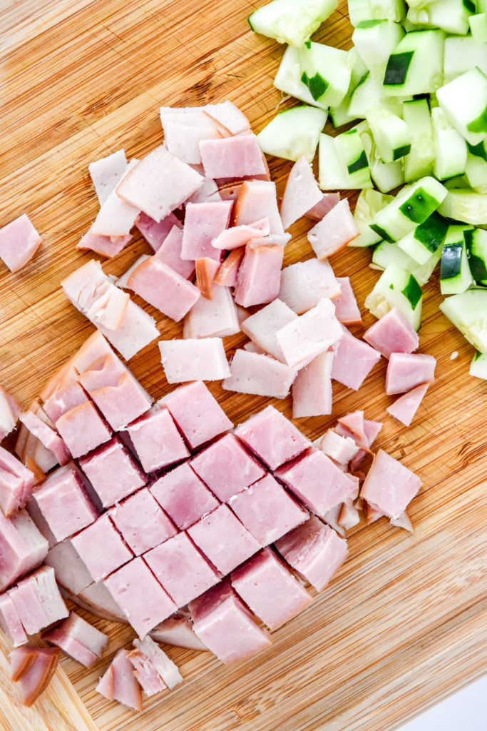 cutting up the ham and cucumber on a cutting board for the easy chef salad meal prep.