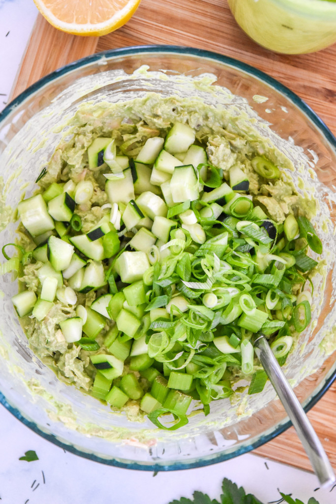 cucumber, onions and celery added to the green sauce and tuna mixture in a glass bowl.