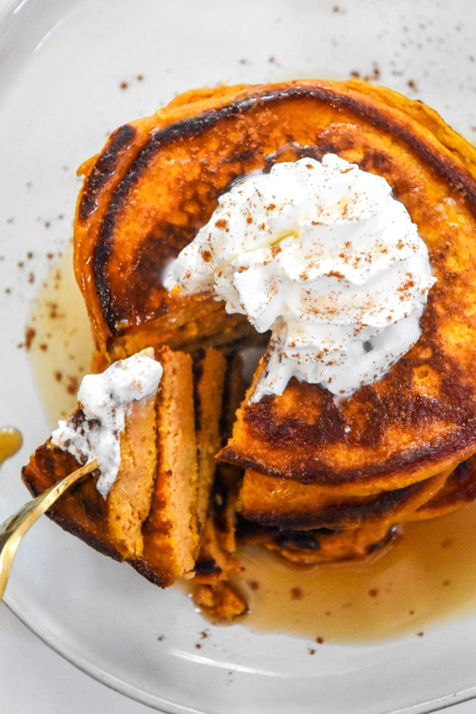Pumpkin pie greek yogurt pancakes on a plate with whipped cream on top.