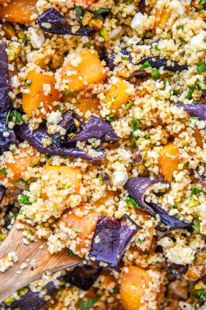 close up of the prepared roasted butternut squash couscous salad with a wooden spoon.