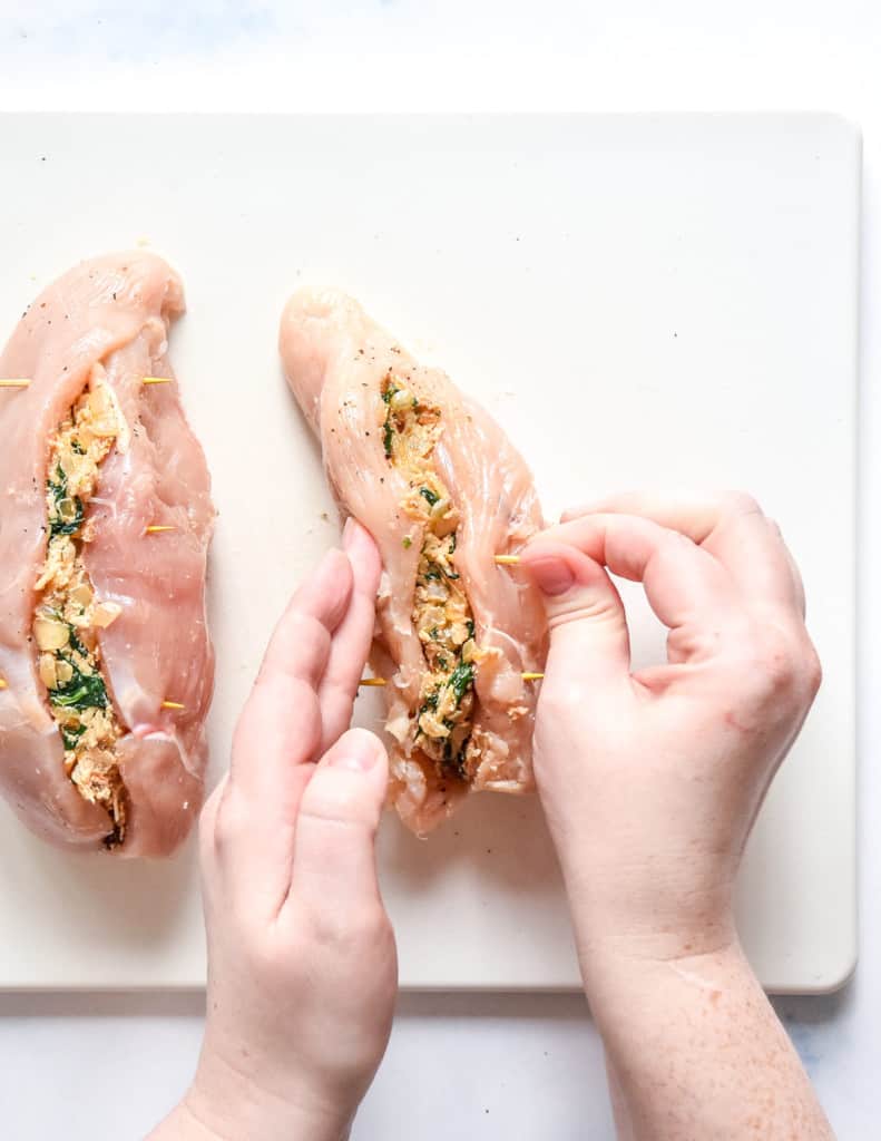 closing the stuffed chicken breasts with toothpicks.