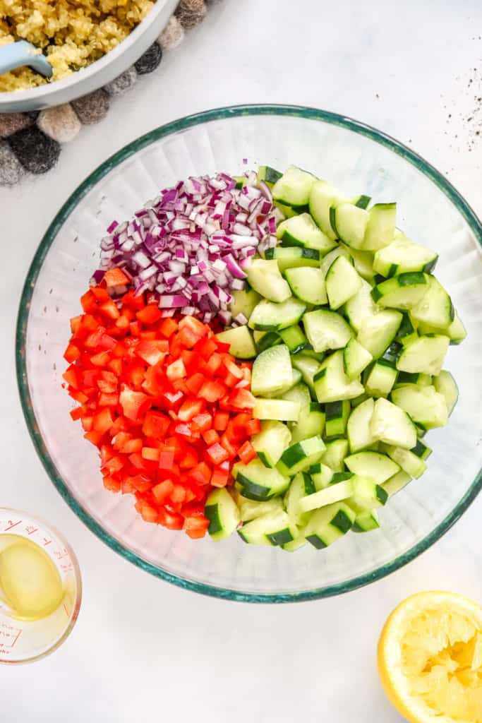 cut cucumbers, red bell peppers, and red onion in a large glass bowl for the make-ahead quinoa party salad.