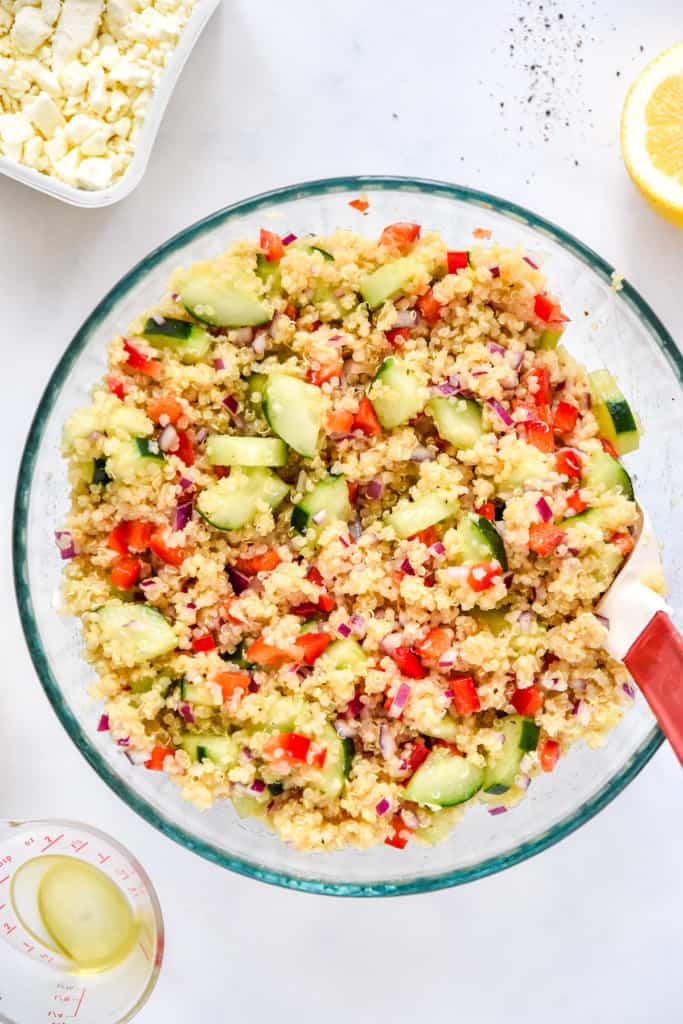 mixed up make-ahead quinoa party salad in a large glass bowl with spatula.