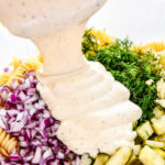pouring dressing into the dill pickle pasta salad bowl.
