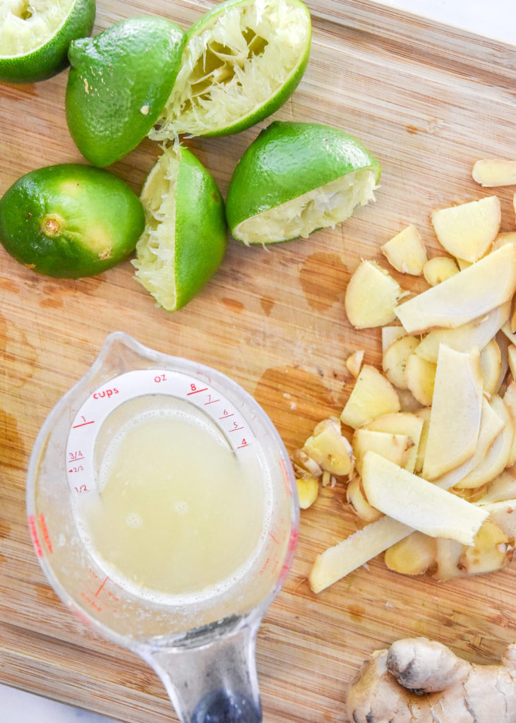 cut limes, fresh lime juice, and sliced ginger on a cutting board.