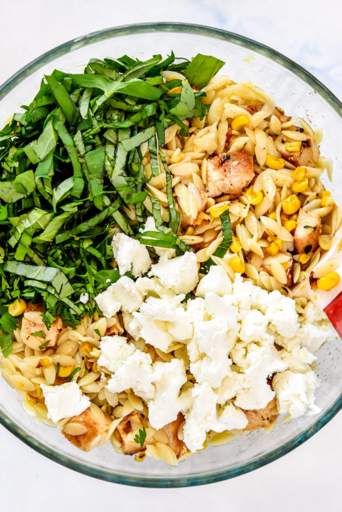 ingredients and herbs in a glass bowl to make the lemony chicken and corn orzo salad.