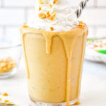 A Peanut Butter Powder Milkshake in a clear cup with whipped cream and chopped peanuts on top.