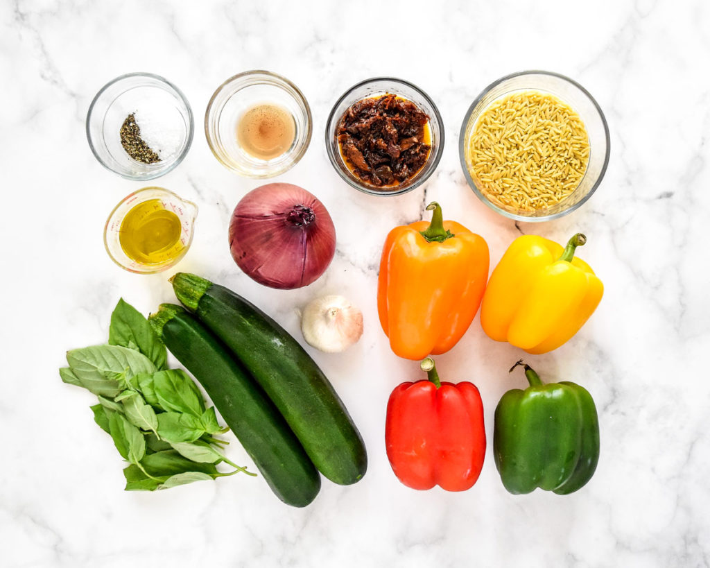 ingredients before starting to make the roasted vegetable orzo salad on a white surface.