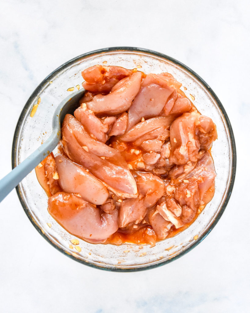 honey sriracha chicken marinating in a glass bowl.