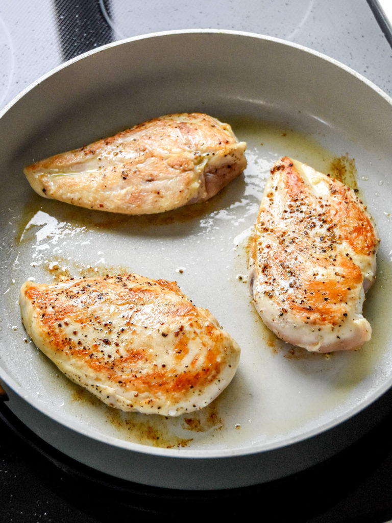 searing chicken breasts in a light colored nonstick pan.