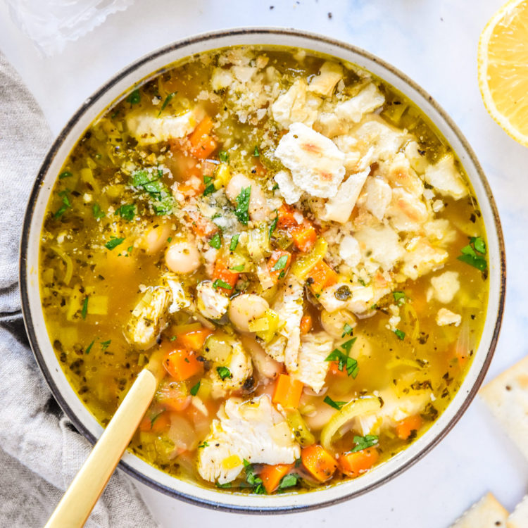 white bean lemon chicken soup in a bowl with saltine crackers on top.