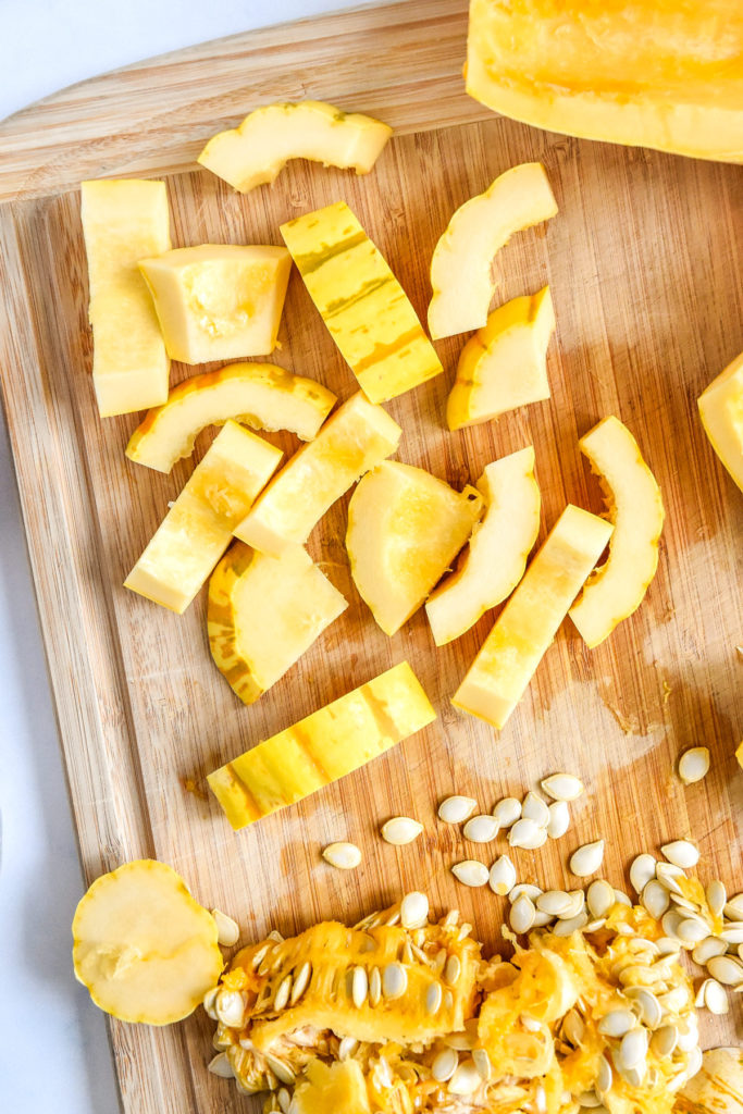 delicata squash cut and deseeded on a wooden cutting board.