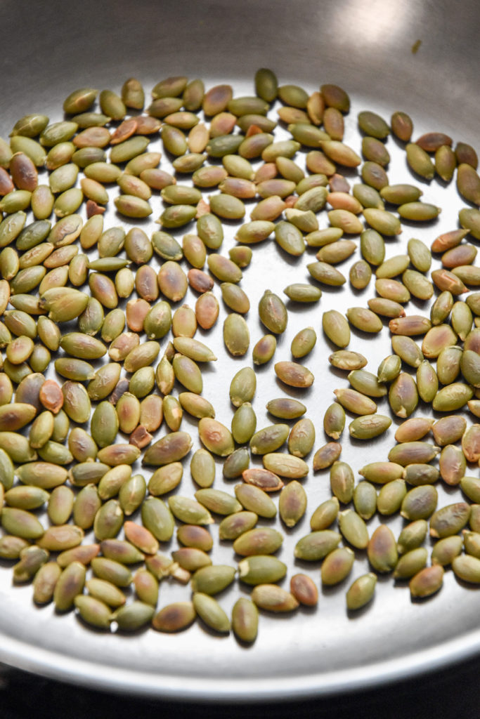 toasting pumpkin seeds in a dry stainless steel pan.