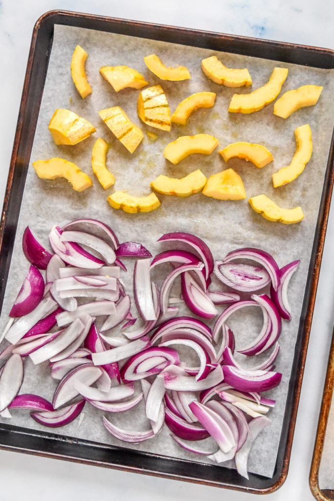 raw squash and onions on a sheet pan before roasting.