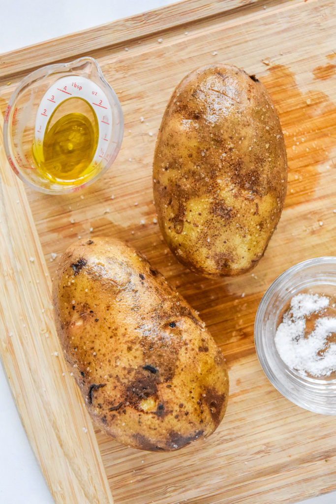 raw russet potatoes covered in oil and salt before baking.